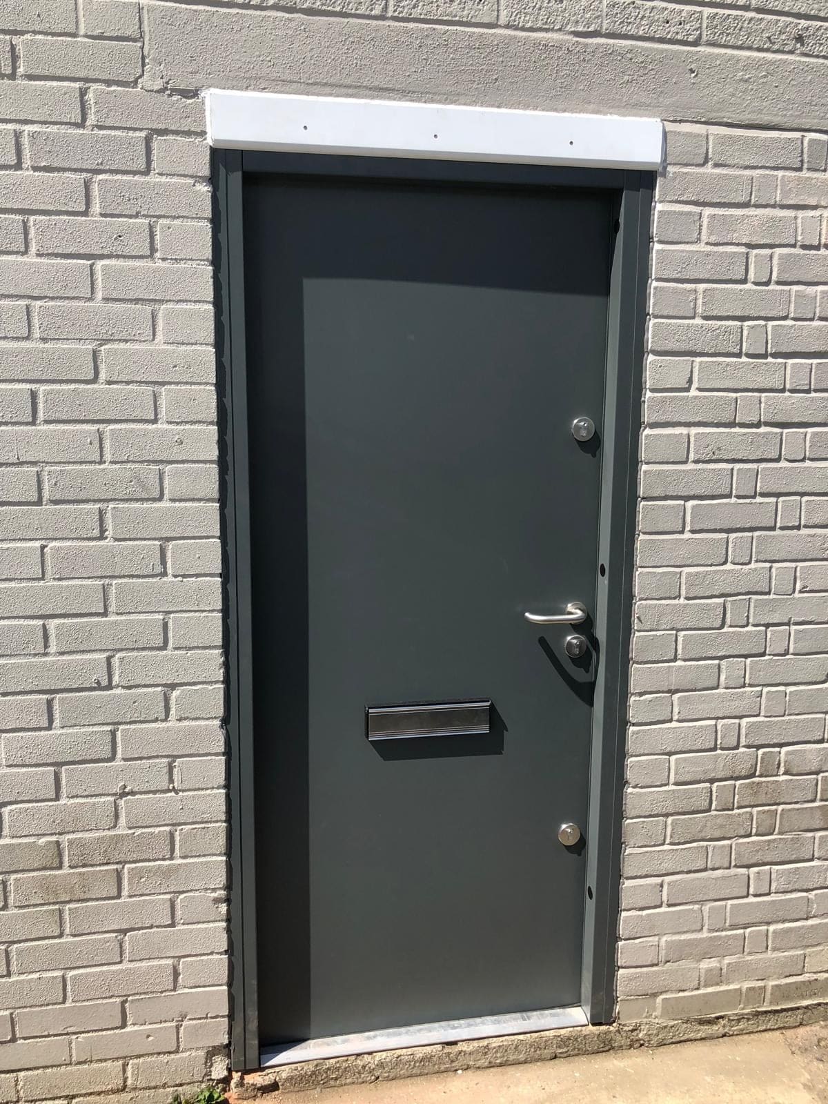 Single-panel green steel fire door on brick wall commercial property