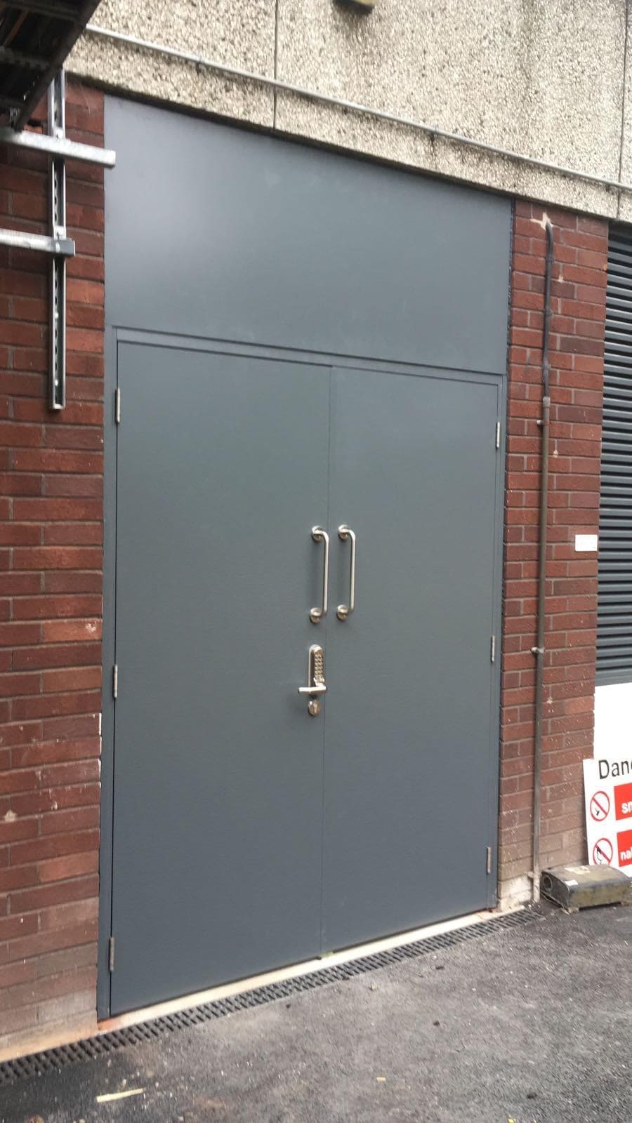 Certified FD-rated steel fire door with teal double panels installed on brick commercial exterior