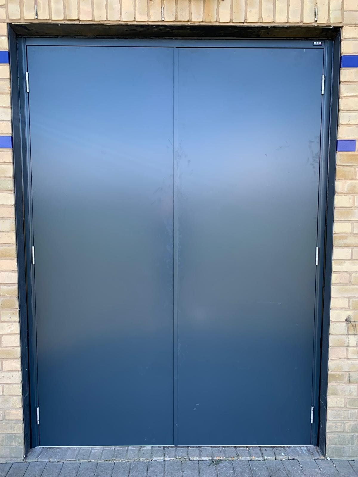 Steel fire door with blue ventilation louvre panels on brick warehouse building